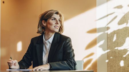 A woman looks toward the window while at her desk at work.