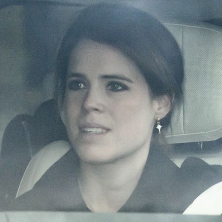 Princess Eugenie sitting in a car wearing a black coat and dangling earrings