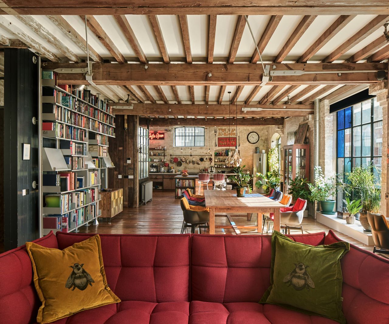 A large open plan kitchen dining room with wooden beam roof and bookshelf wall