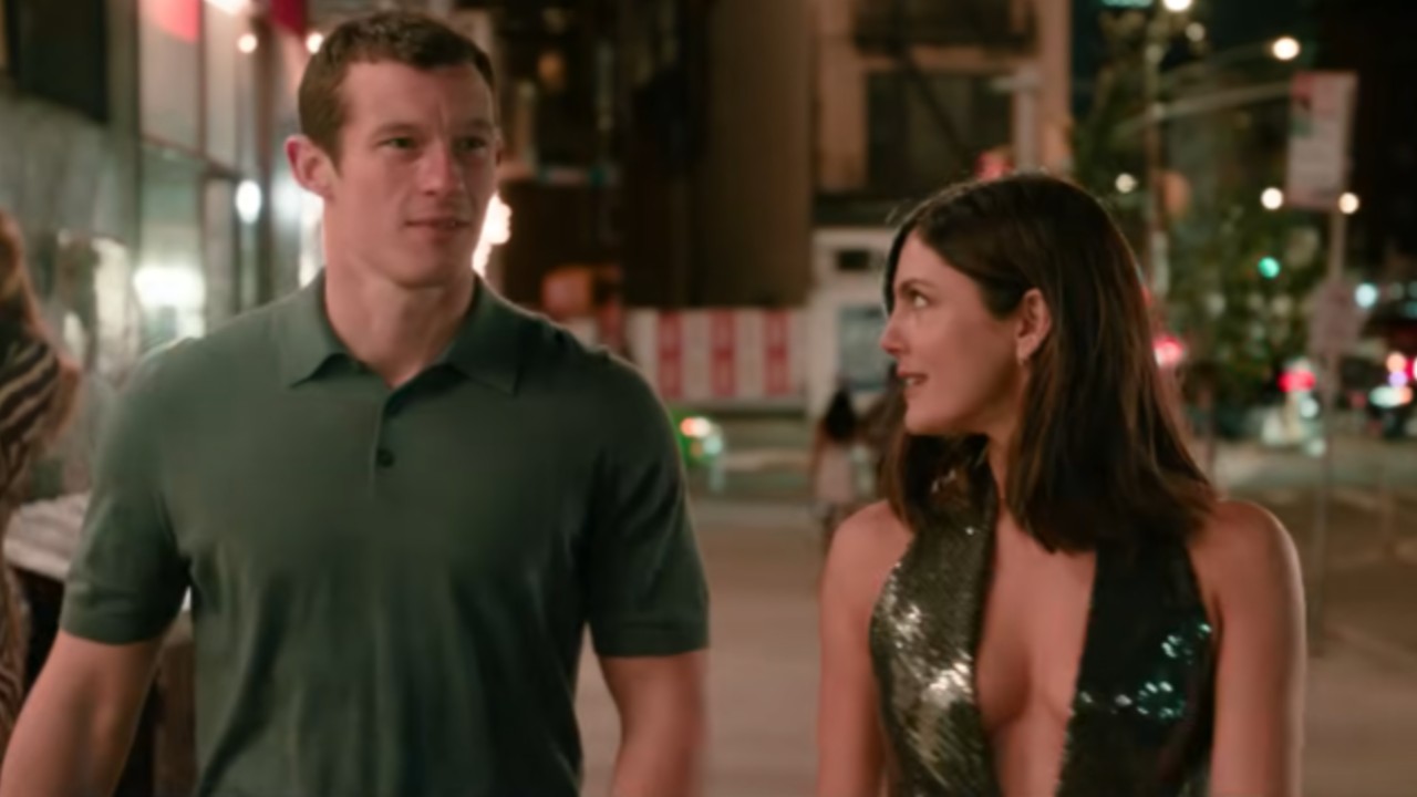 From left to right: Callum Turner looking forward and Monica Barbaro looking to her left at him as they walk down the street in One Night Only. 