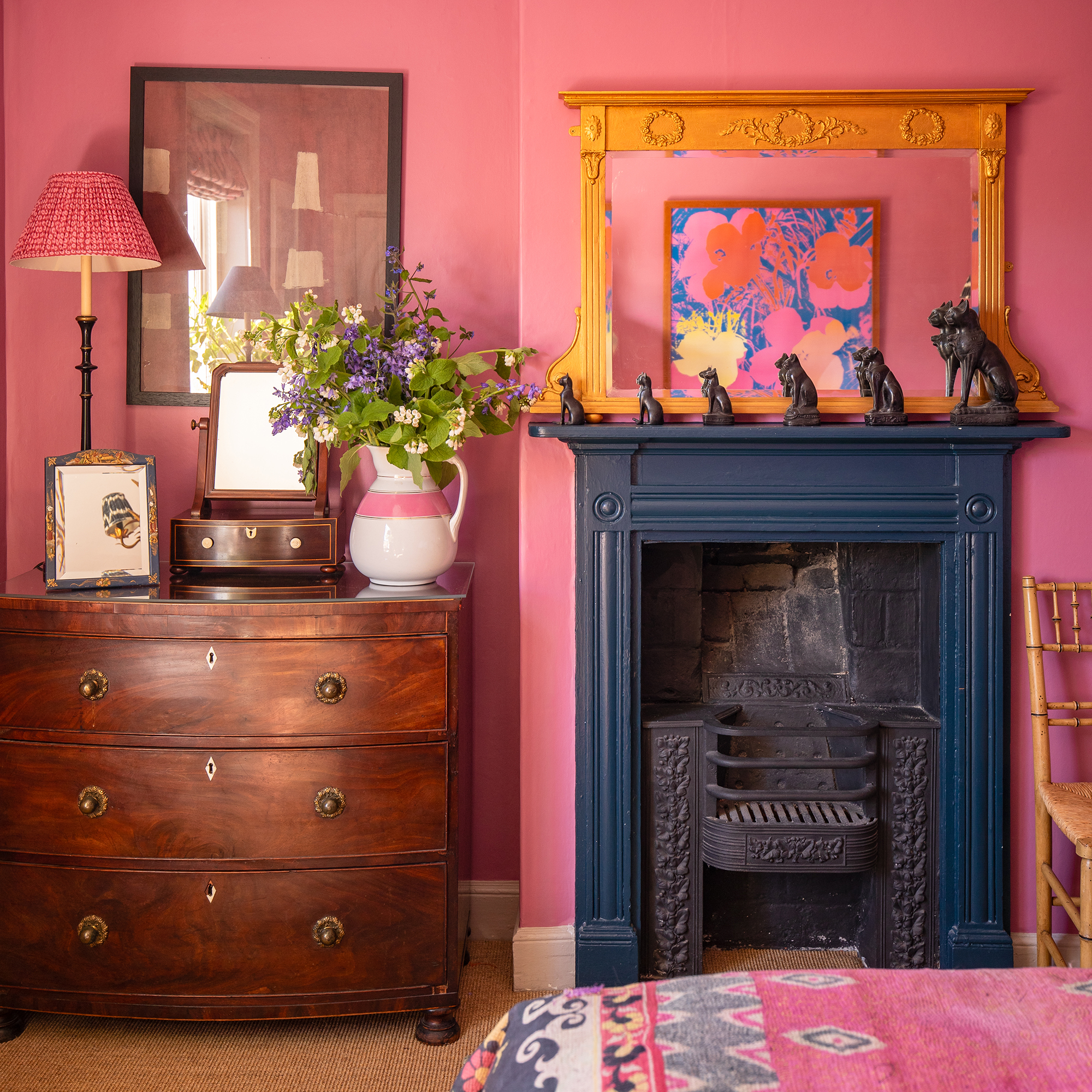 bright pink painted bedroom with antique furniture and dark blue painted georgian fireplace