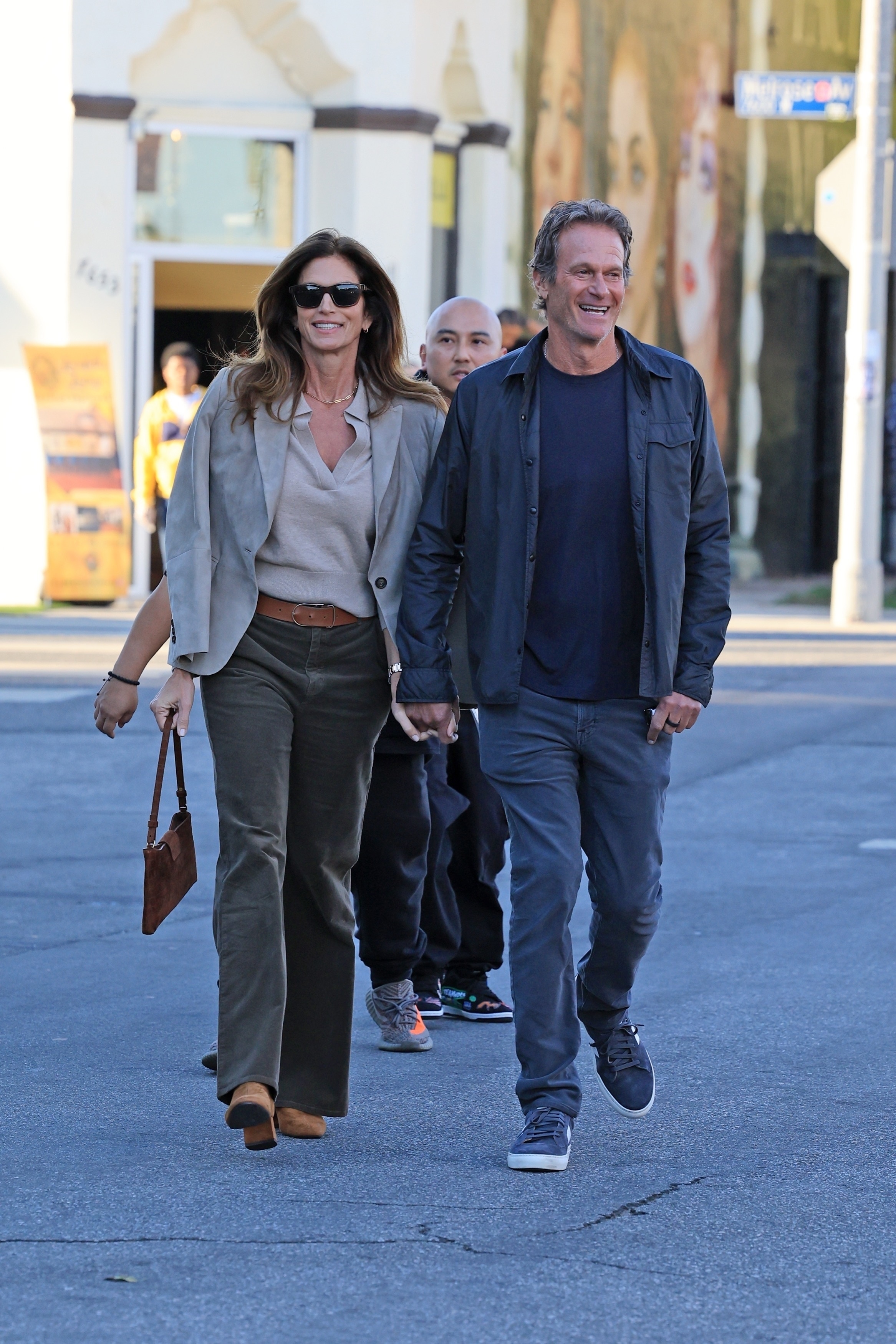 Cindy crawford wears corduroy pants, suede boots, a suede bag, gray blazer and beige sweater.