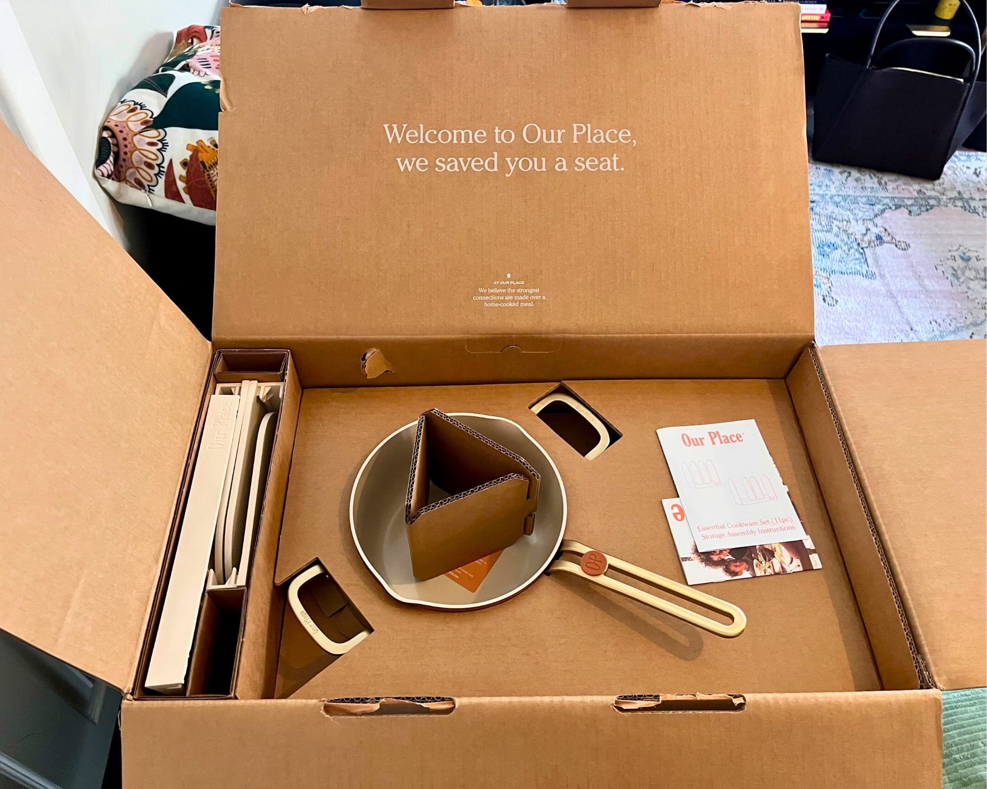 The open package of the Our Place 11-Piece Essentials Cookware Set delivery. It shows neatly packed pans with cardboard-only packing and no plastic. There are two cards with information from the brand on top.