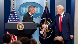 Two men wearing suits shake hands behind a podium