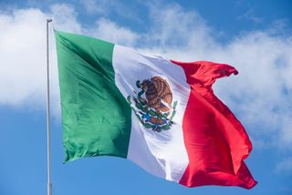 The flag of Mexico waving against blue cloudy sky