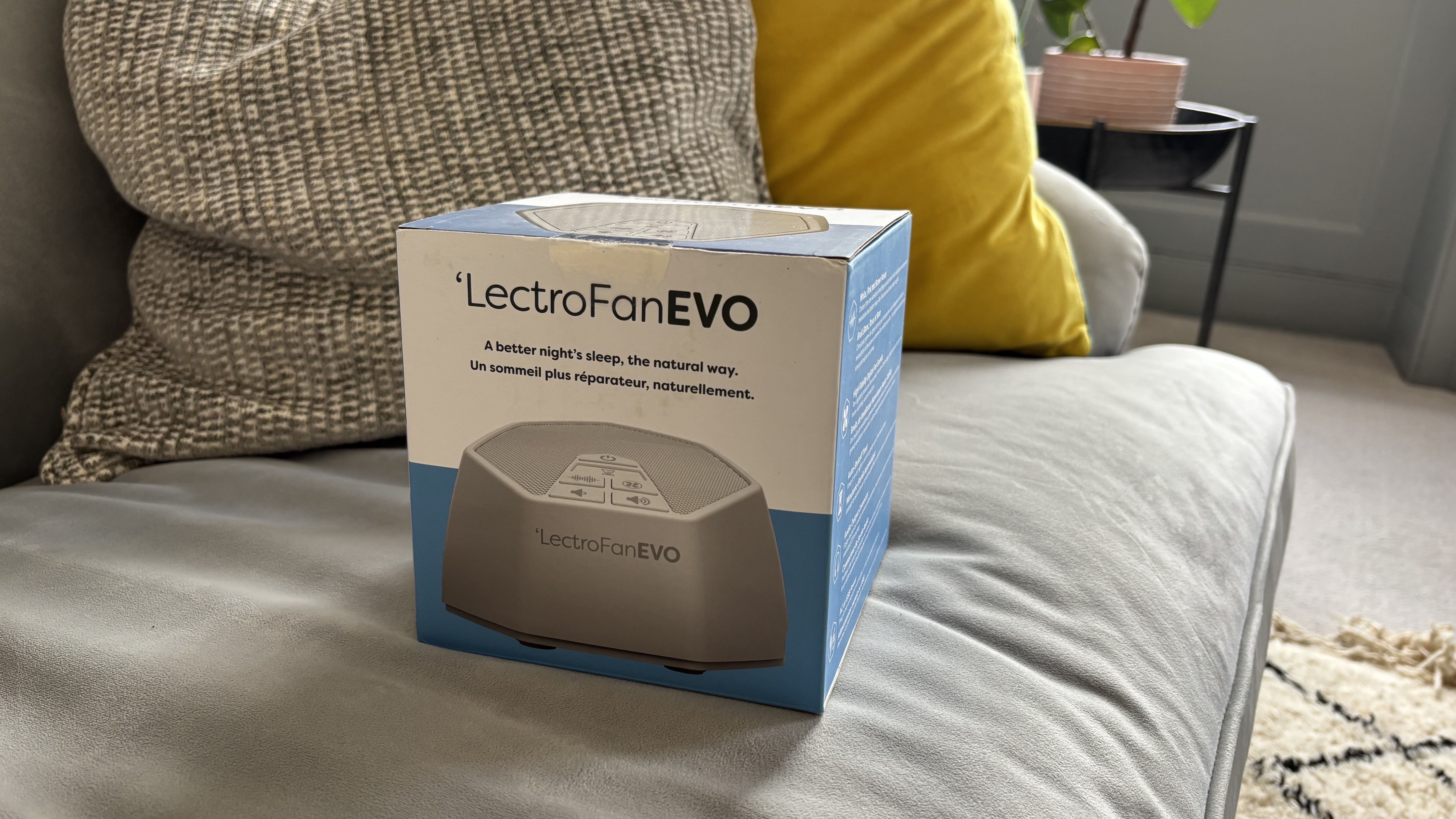 The blue-and-white box containing the LectroFan EVO White Noise Machine on a couch.