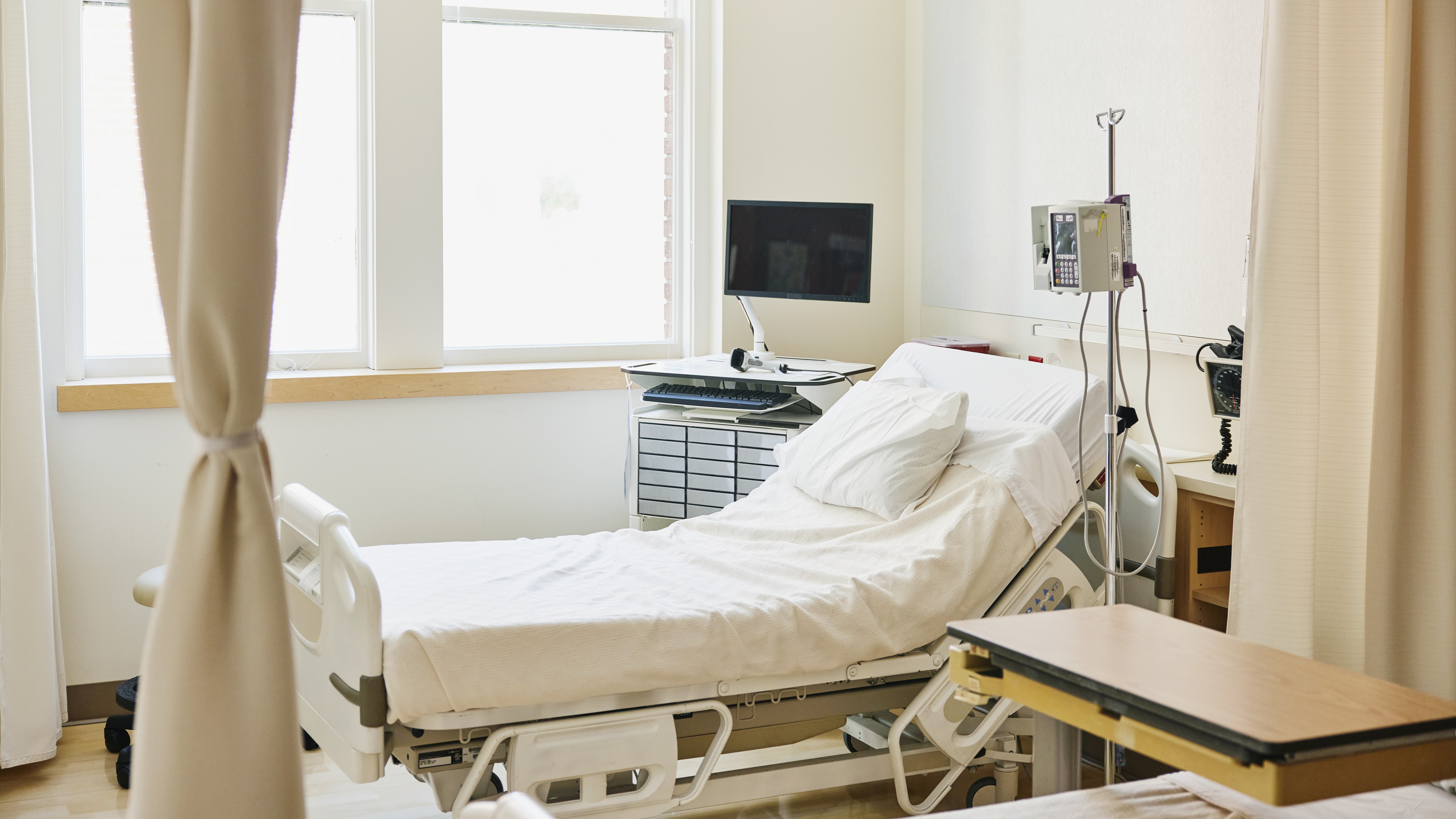 an empty hospital room with a bed, IV stand, curtain and monitors