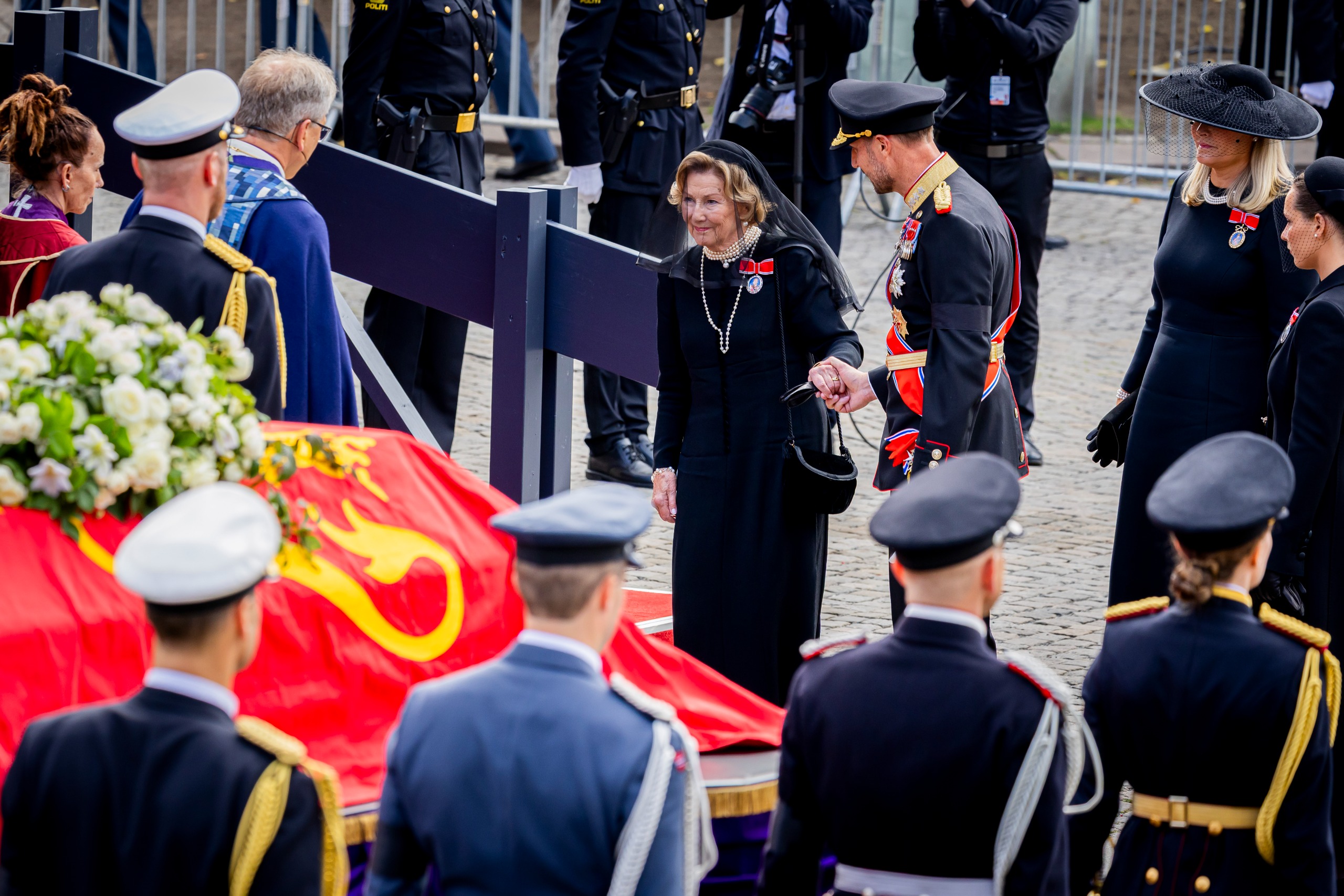 Queen Sonja holding hands with King Haakon at King Harald's funeral
