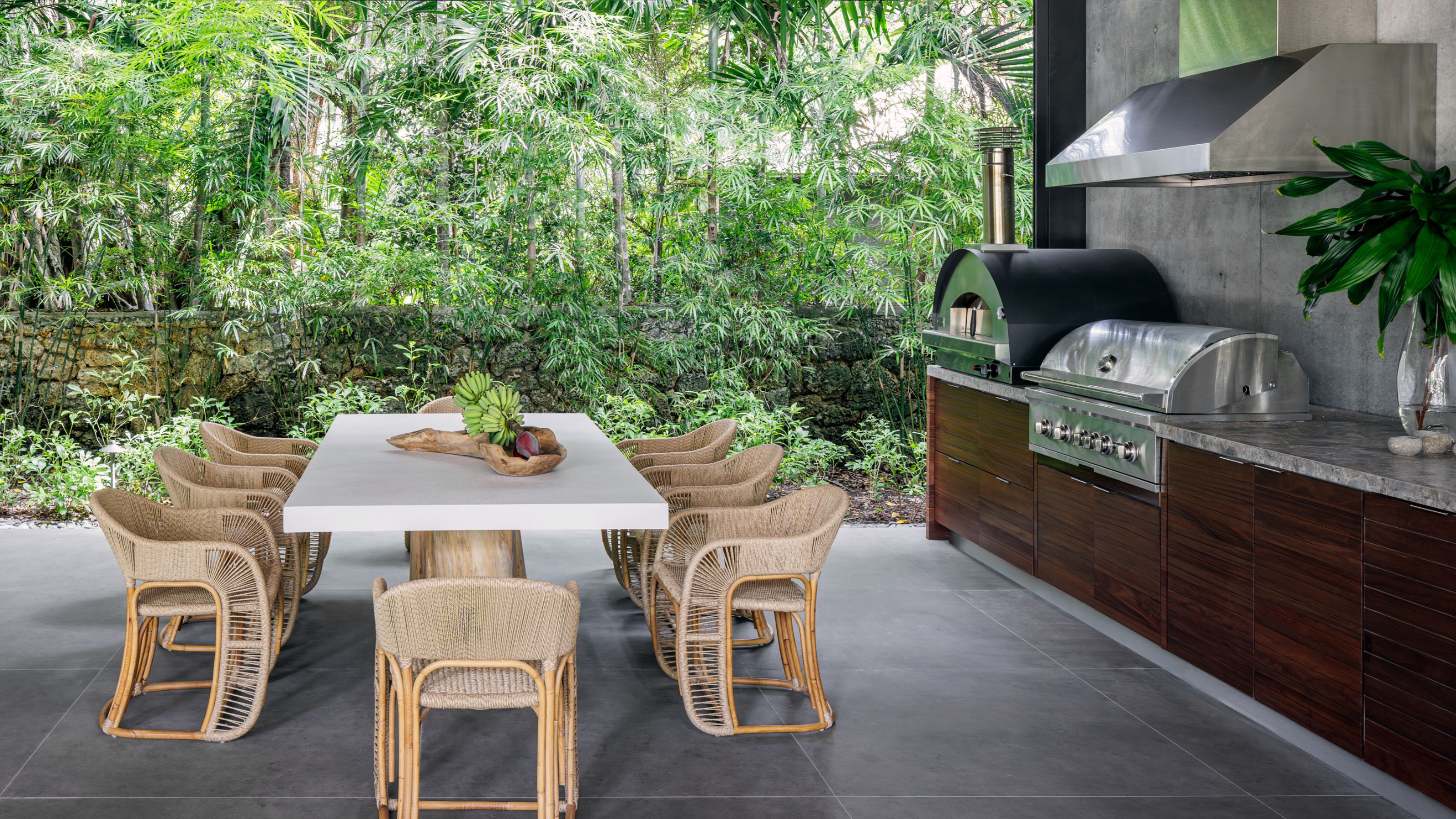 An outdoor kitchen with built-in grill, an oven and a dining table set up 