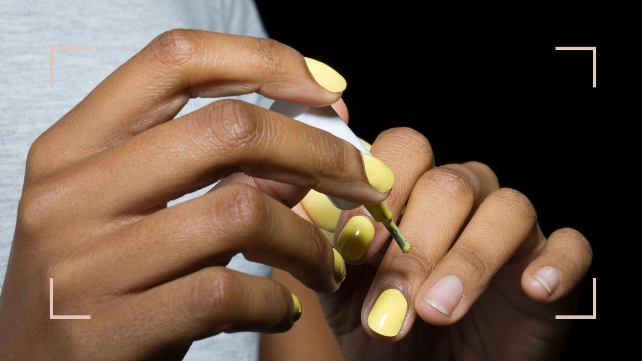 A woman&#039;s hands painting her nails yellow and learning how to dry nail polish fast 