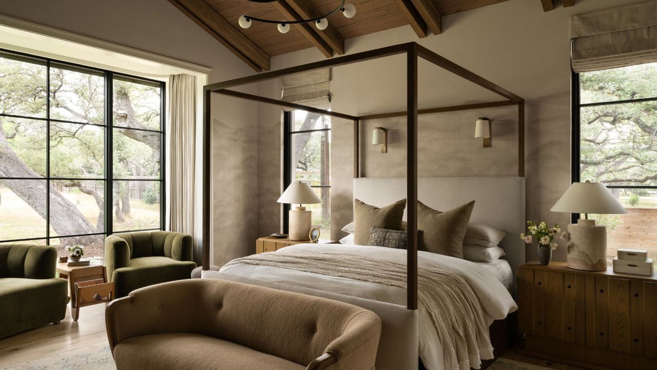 Neutral bedroom with four poster, wooden beams, brown sofa and green armchairs