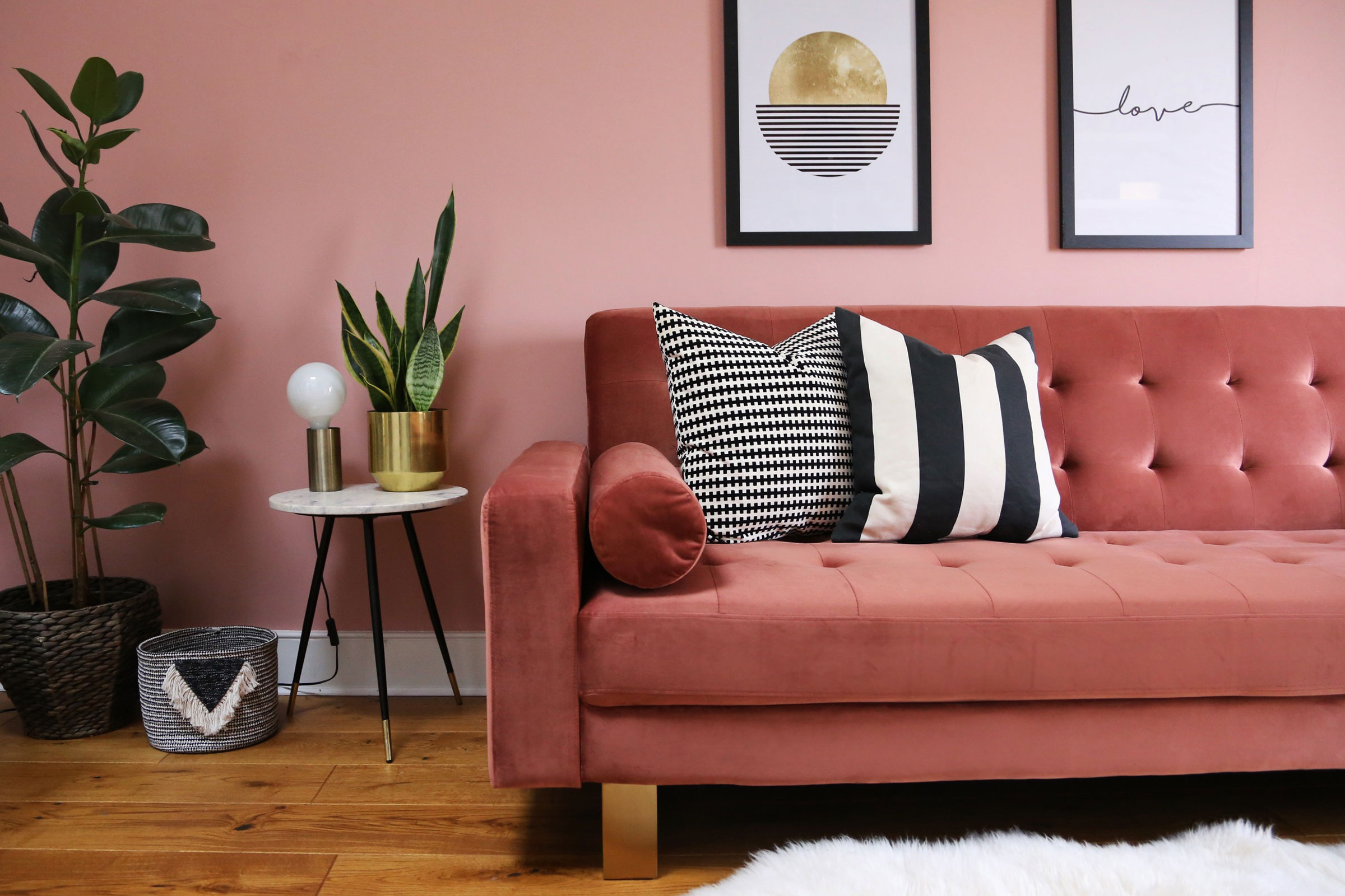 A salmon pink velvet sleeper couch in a small pink living room with pot plants and monochrome accents.