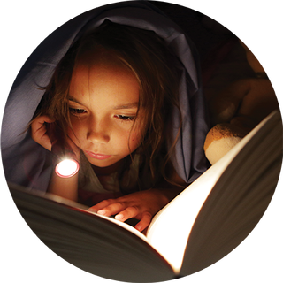 Image of young girl reading a book under the covers with a torch light