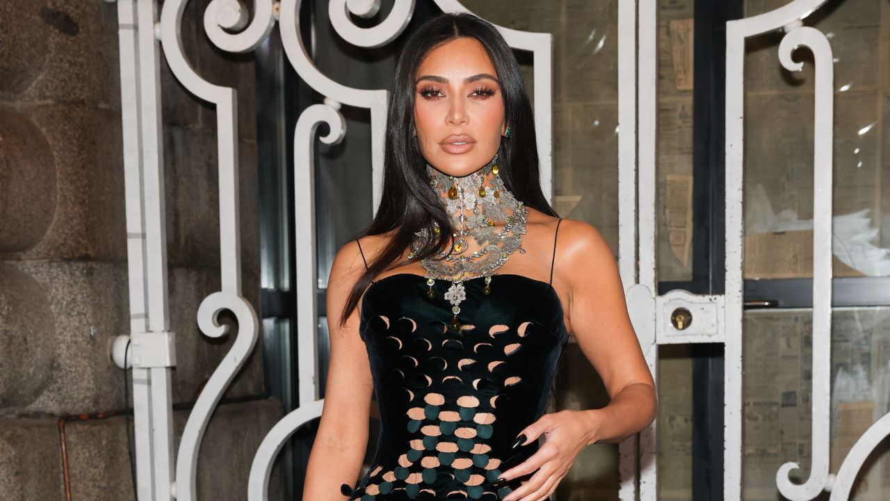 Kim Kardashian stands on a step and repeat wearing a cutout dress