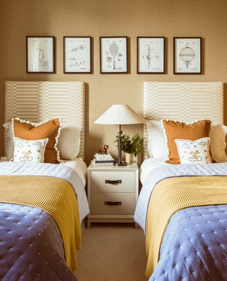 yellow bedroom with twin beds, bedside in the middle, artwork, upholstered headboards, blue throws at end