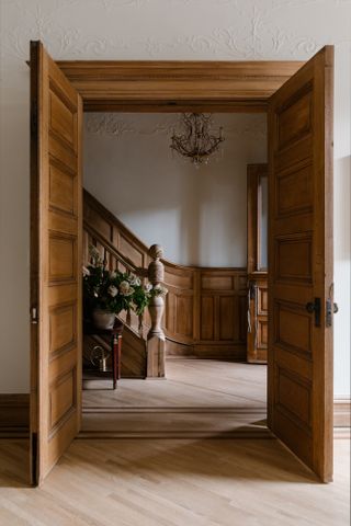 The wood panelled entryway to a brownstone property with a staircase and doors opening into a further room