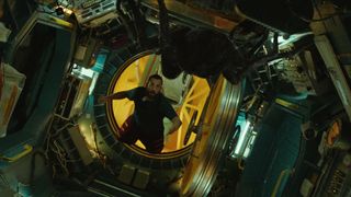 a man floats in zero gravity inside a cramped spacecraft while looking at a giant spider