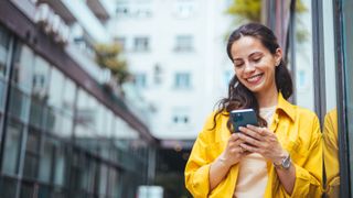 A woman by a business-looking building using a phone and smiling