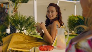 Olivia Wilde in a yellow dress holding a drink in Don't Worry Darling.