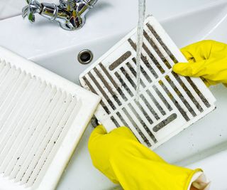 Person in a protective rubber glove washes in the sink air filter of the ventilation return duct blocked by dust and debris.