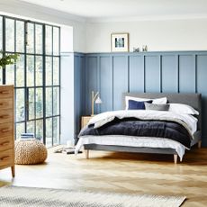 bedroom with blue panel wall grey bed with designed cushion bifold glass door and wooden flooring