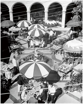 Black and white photograph of a courtyard with tables covered by patterned parasols