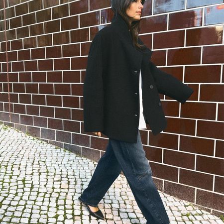 Model wearing a high-neck coat with jeans and flats. 