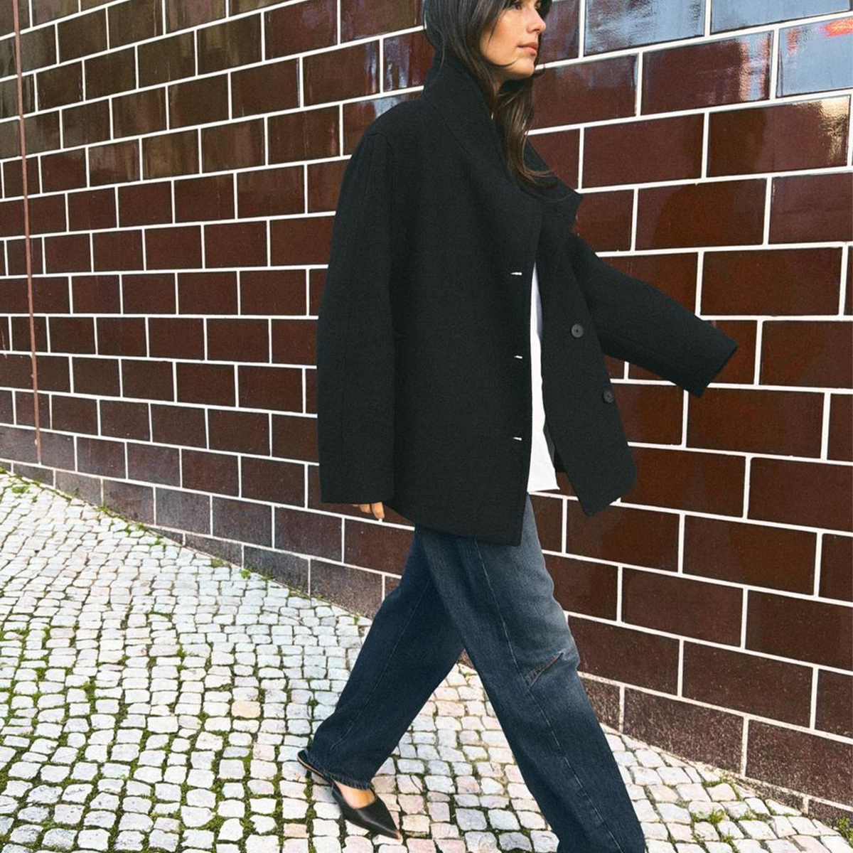 Model wearing a high-neck coat with jeans and flats. 