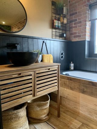 A bathroom idea with exposed brick wall, wooden vanity and black wall paneling decor