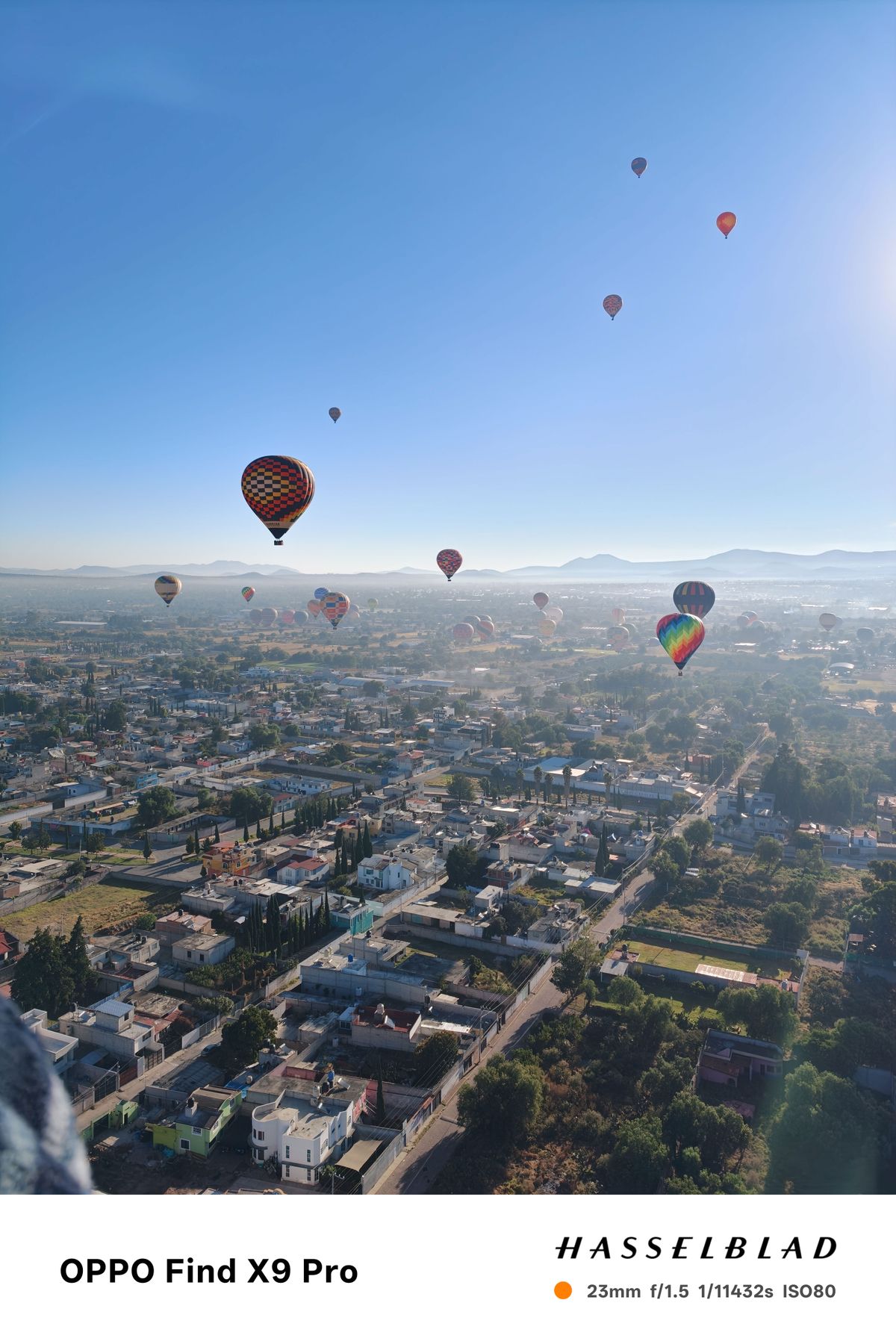 Hot air balloons floating above a village in Mexico in front of a clear blue sky