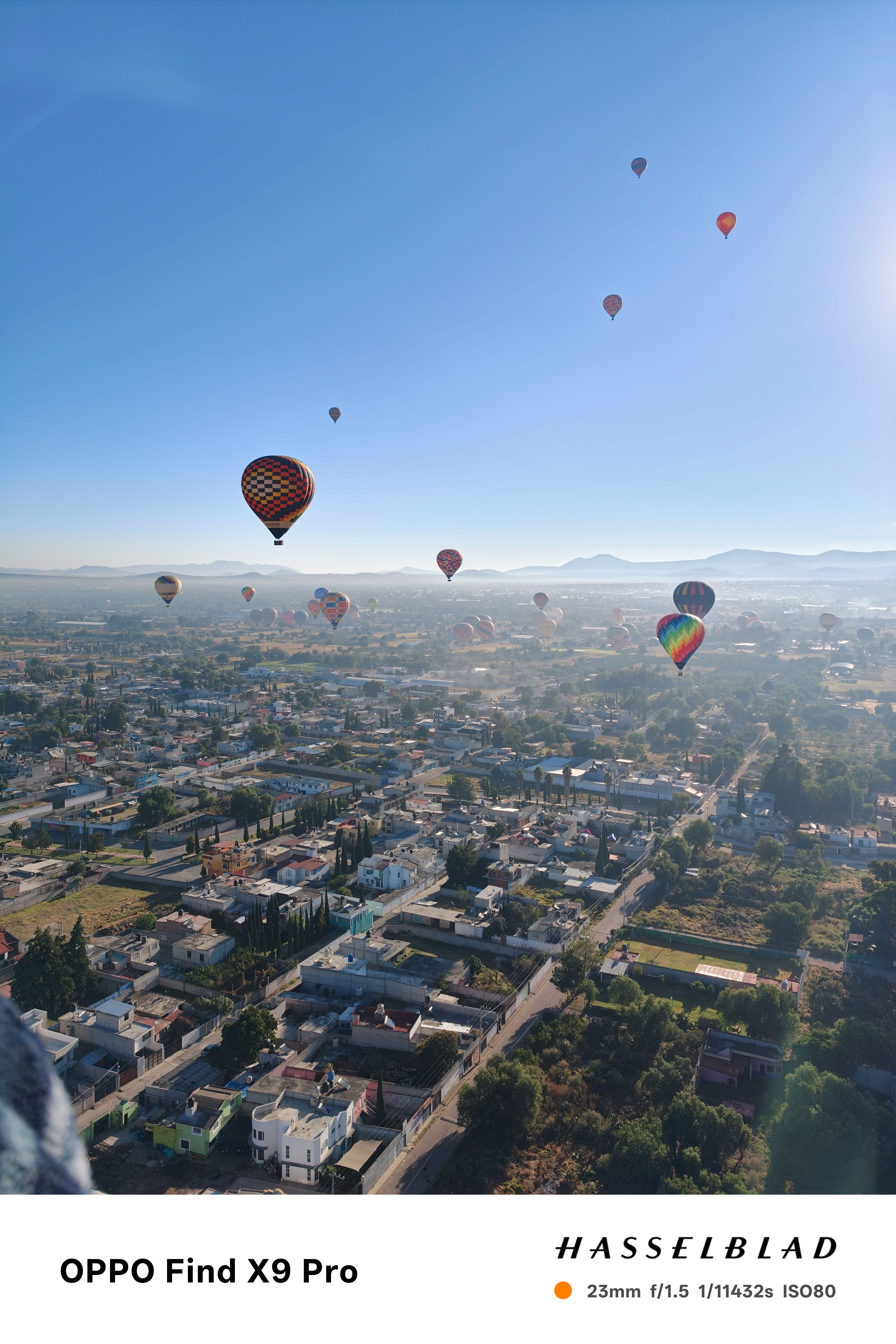 Hot air balloons floating above a village in Mexico in front of a clear blue sky