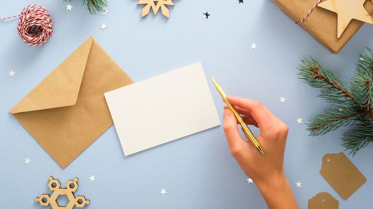 A woman thinking about what to write in a Christmas card in front of a blank piece of paper, brown envelope, string and wooden star decorations