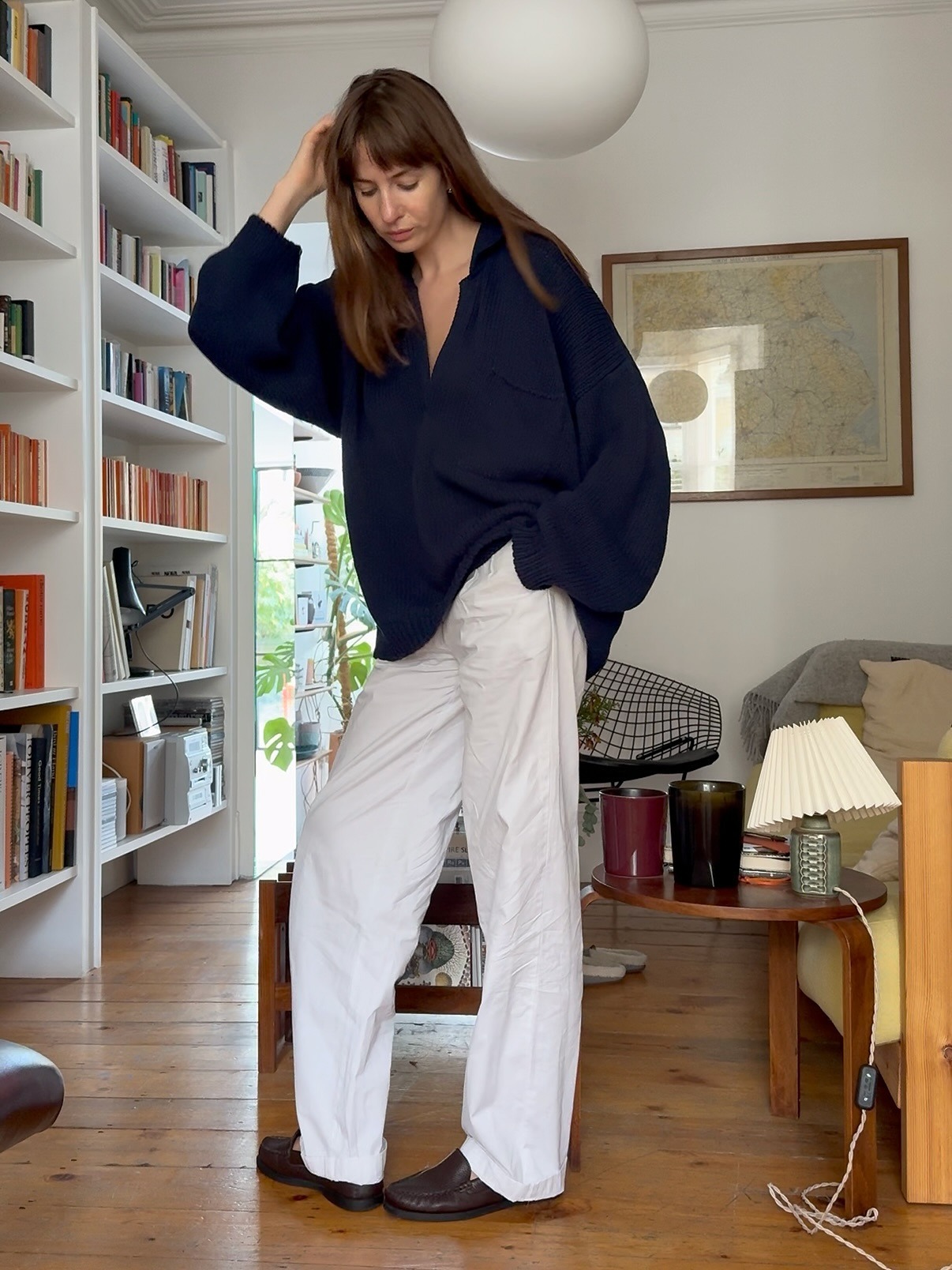 Influencer @lizzyhadfield wears a navy v-neck jumper with white jeans and dark brown loafers.