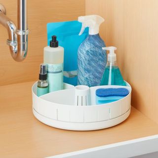 White turntable under sink with toiletries and cleaning supplies.