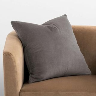 A gray velvet throw pillow in the corner of a brown couch