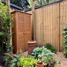 Wooden garden wardrobe in a garden with a wooden fence and pots filled with plants