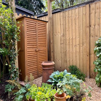 Wooden garden wardrobe in a garden with a wooden fence and pots filled with plants