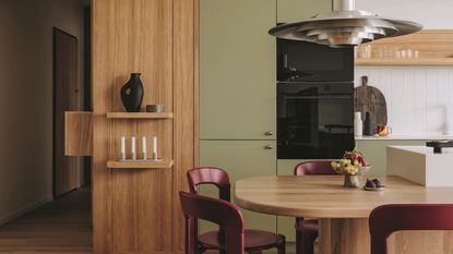 matcha green and timber kitchen with burgundy chairs around a timber island bench with a chrome pendant light hanging over and white fluted backsplash