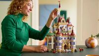 A woman places a brick onto the Lego Beauty and the Beast Castle, which sits on a dark table