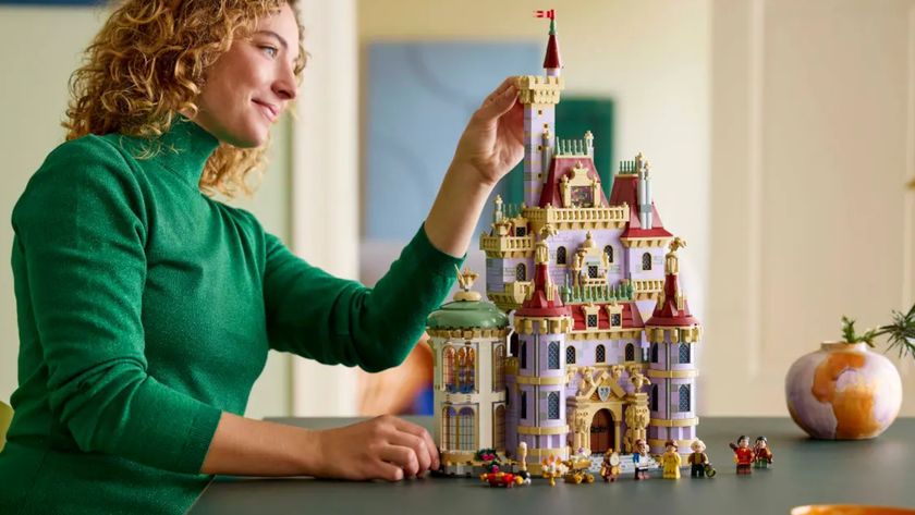 A woman places a brick onto the Lego Beauty and the Beast Castle, which sits on a dark table