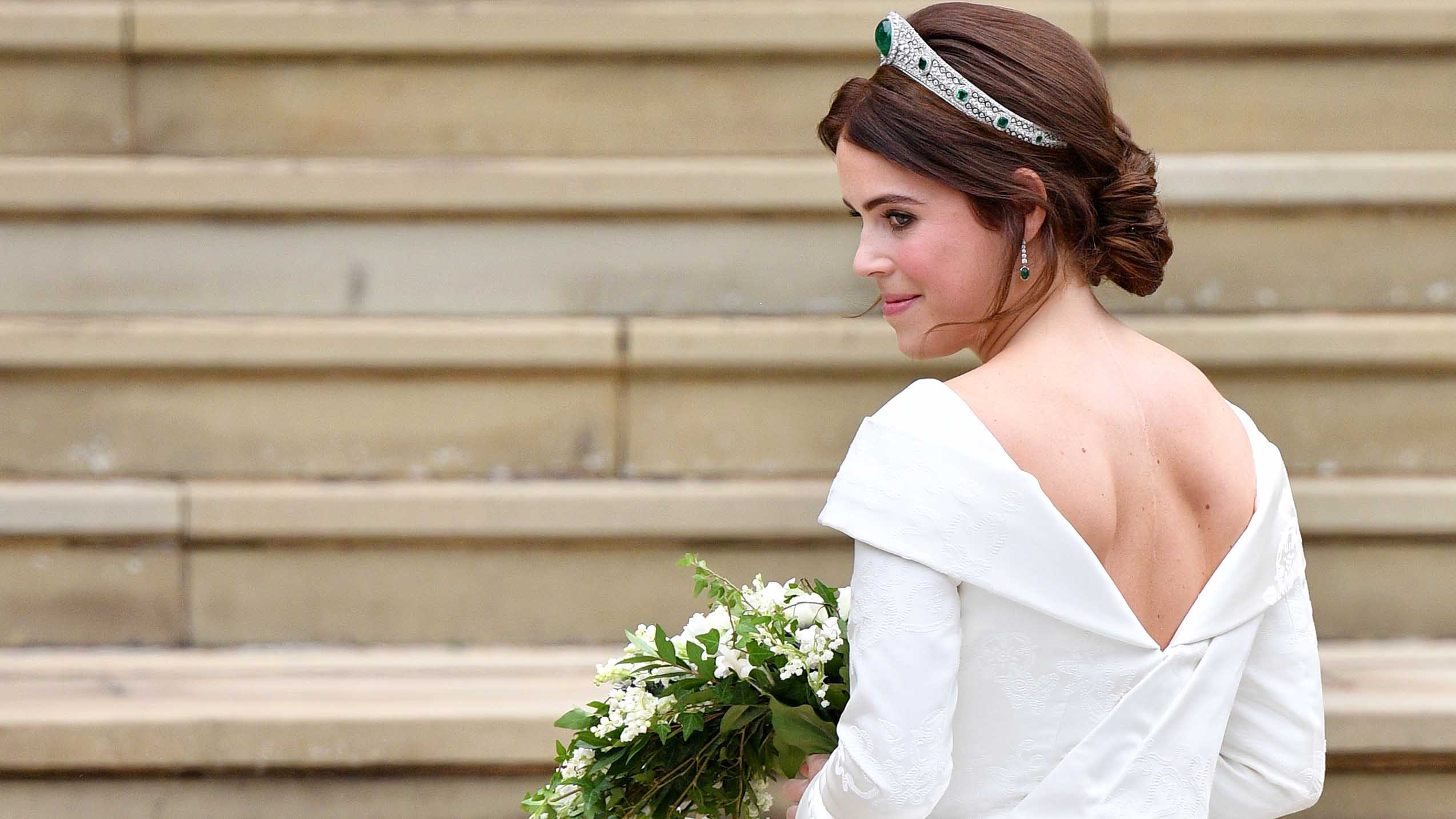 Princess Eugenie at her wedding, wearing a white wedding dress with a v-cut back and a diamond and emerald tiara