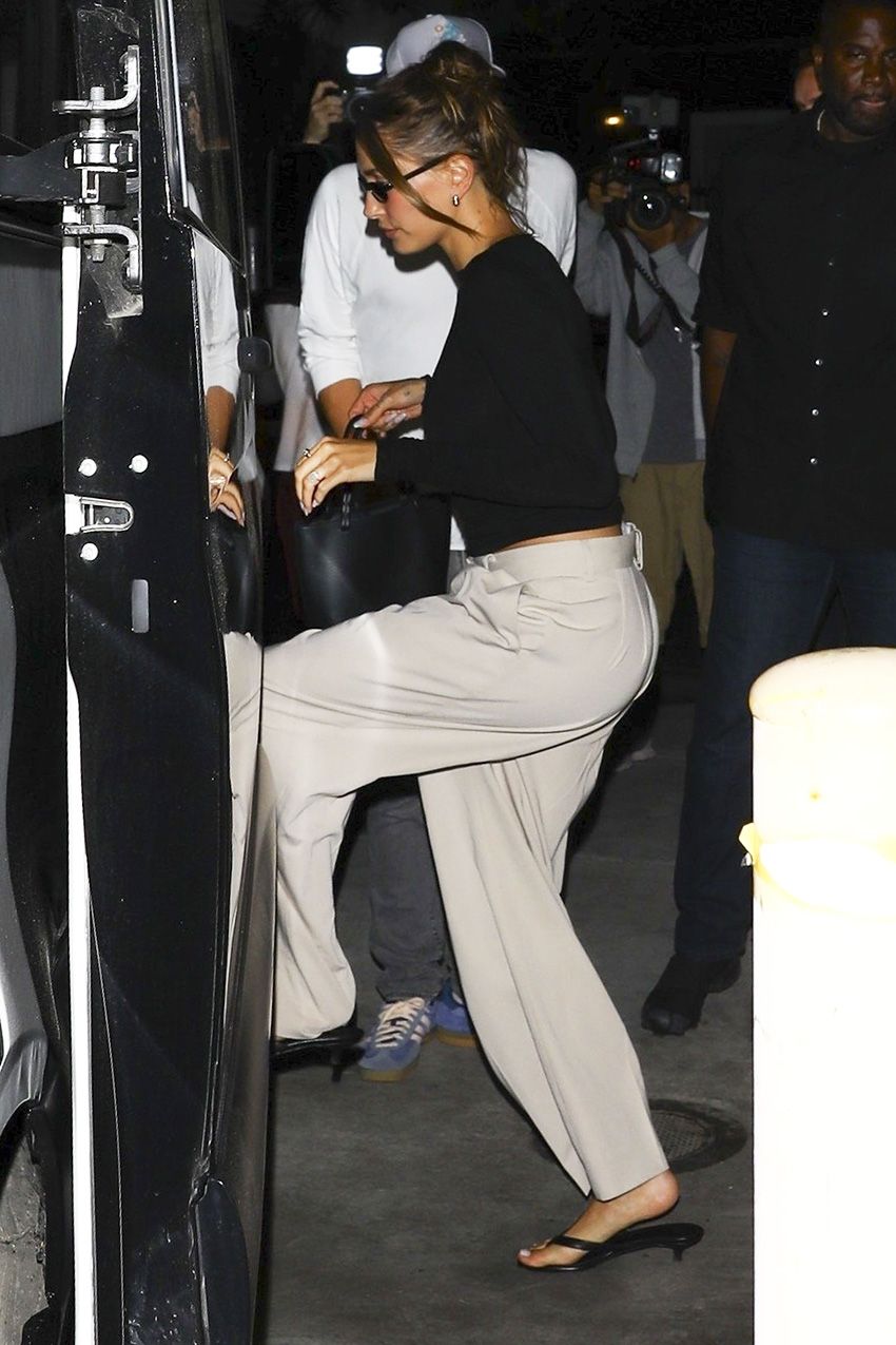 Hailey Bieber wearing a black long-sleeve top, khaki pants, and kitten-heel thong sandals