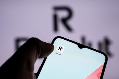 A person is holding a mobile phone with the Revolut application in front of a screen displaying the Revolut logo.