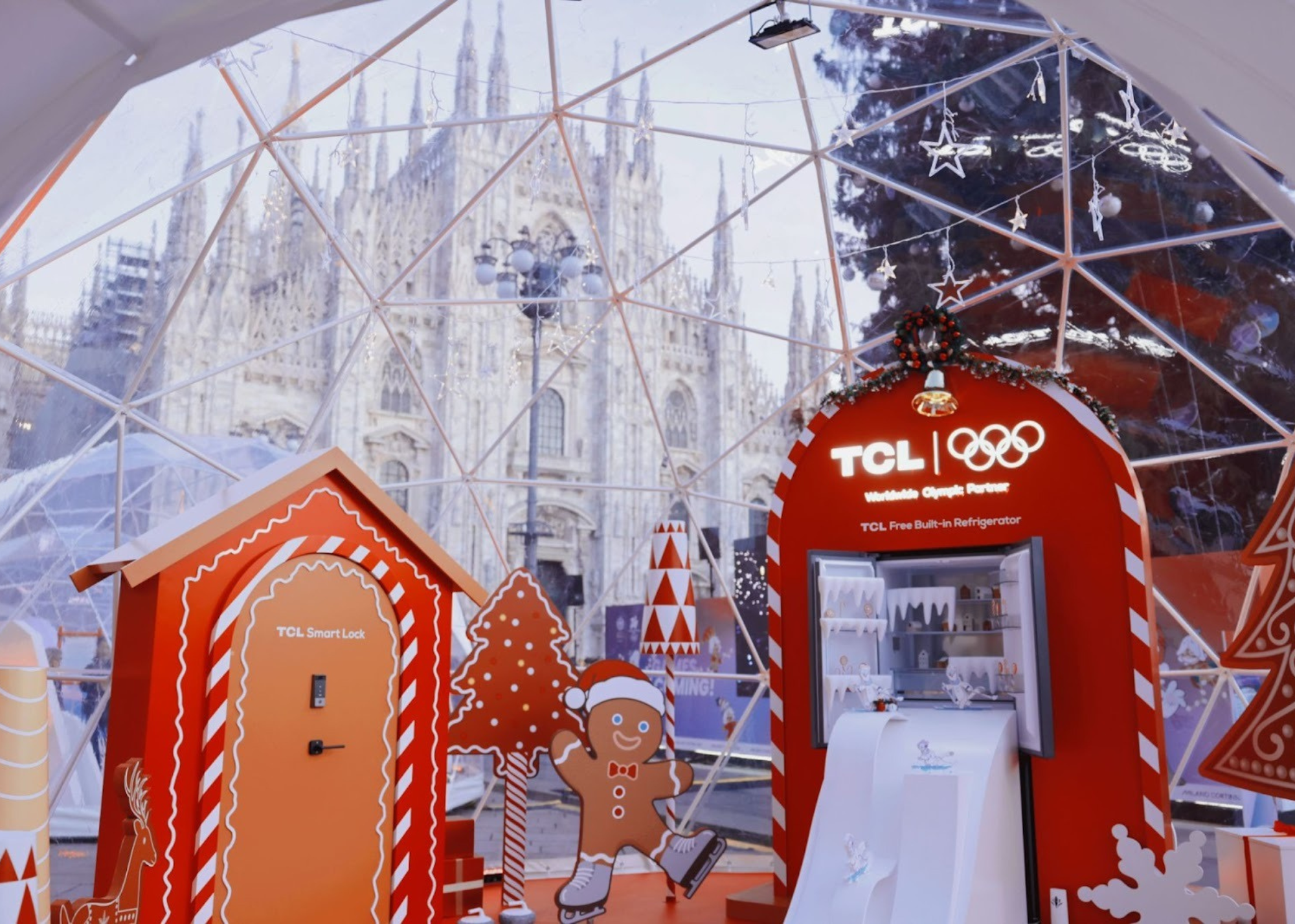 A transparent igloo-style installation with Christmas-themed decor including a fridge with crafted ski slopes