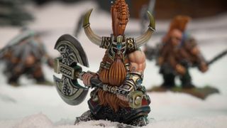A dwarf with a giant mohawk stands holding an axe on a snowy battlefield