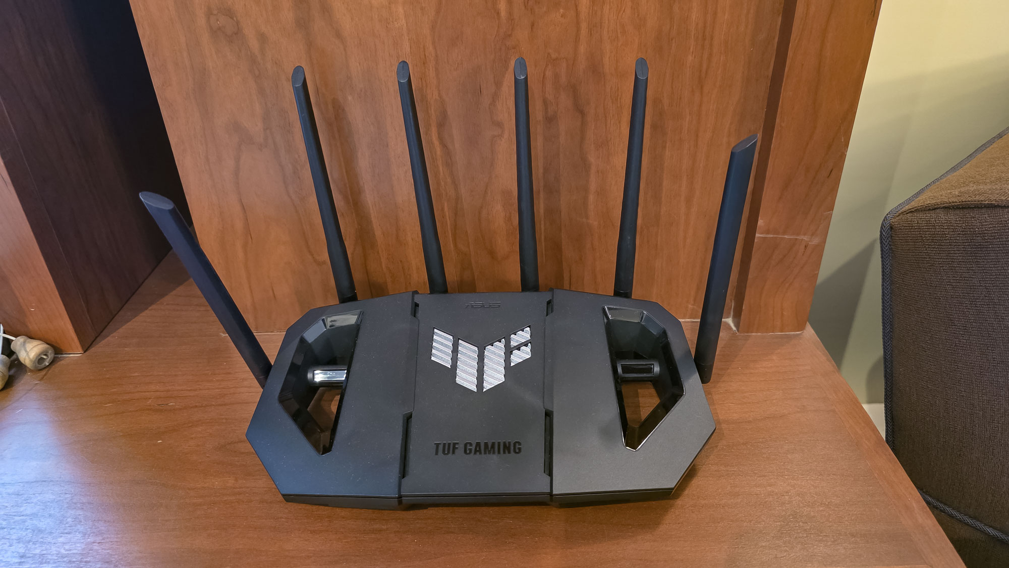 An Asus TUF Gaming BE6500 router on a wooden cabinet.