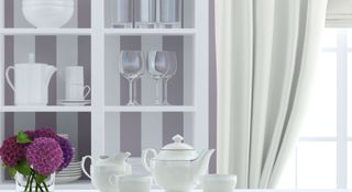 White and lilac wallpaper on a dresser unit with a white tea set in foreground