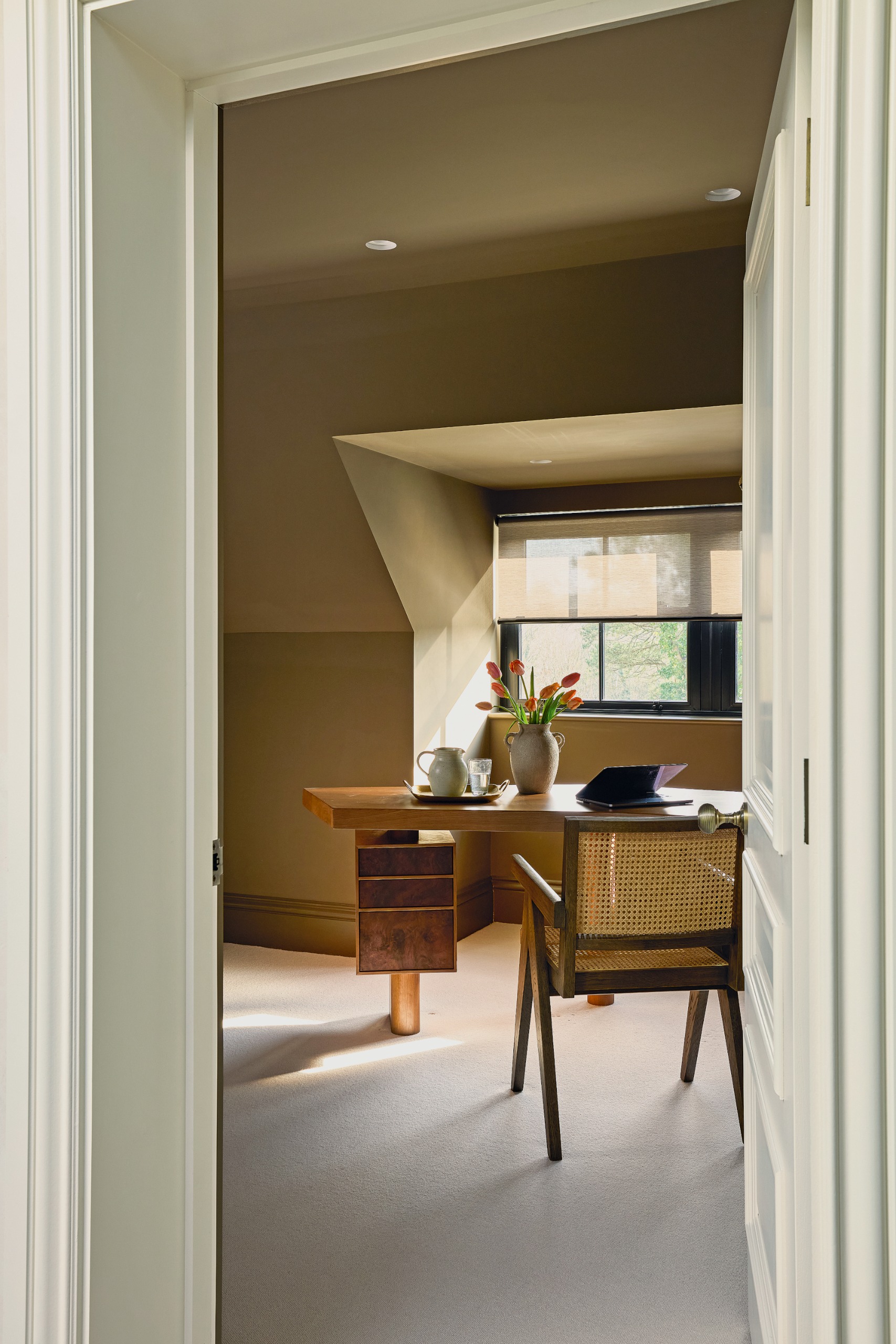 Gray-brown study in the eaves with wooden angular desk, wood and cane chairs and spotlights