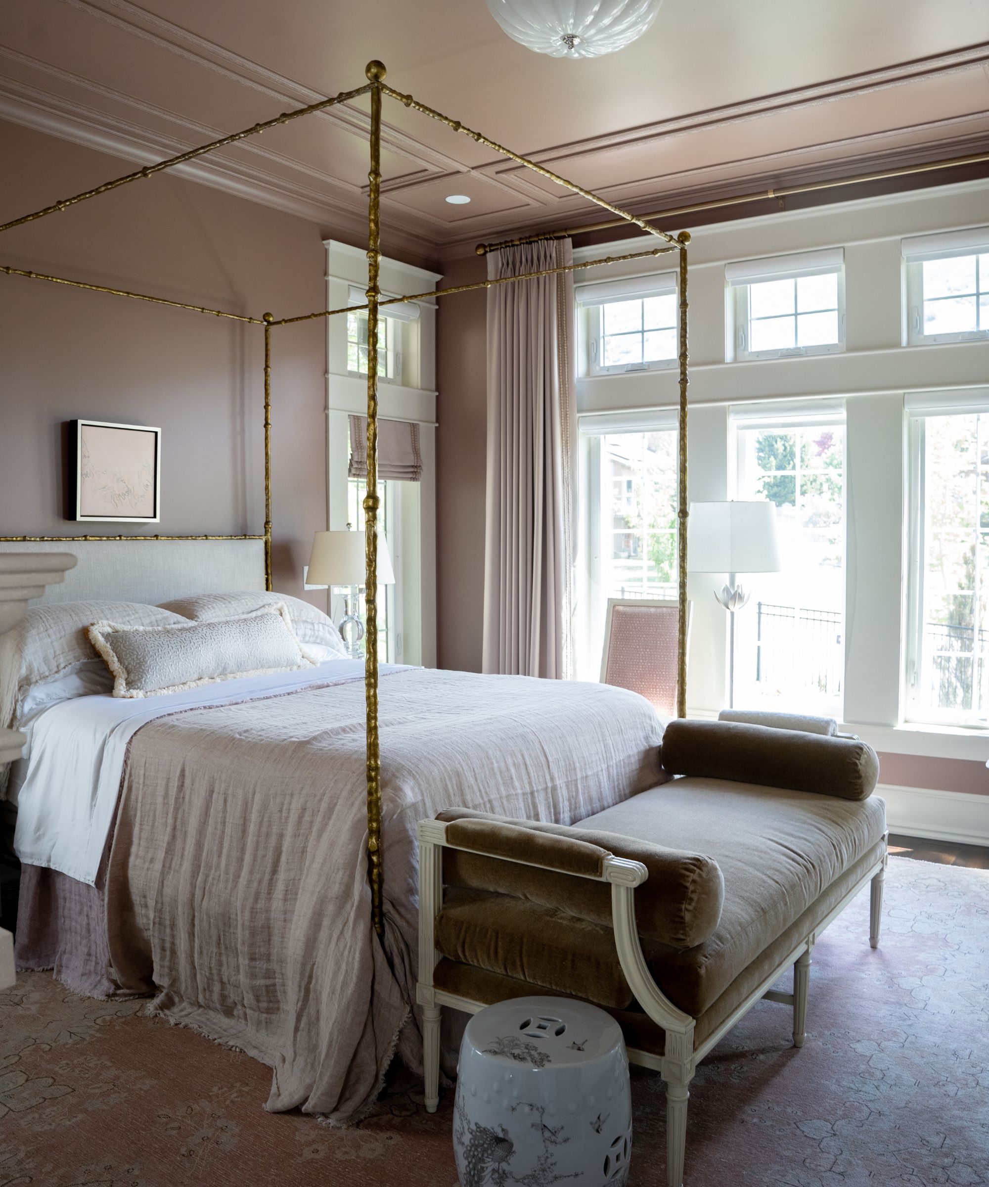 A bedroom with mauve walls and ceiling, a four-poster bed with neutral bedding and transitional decor.