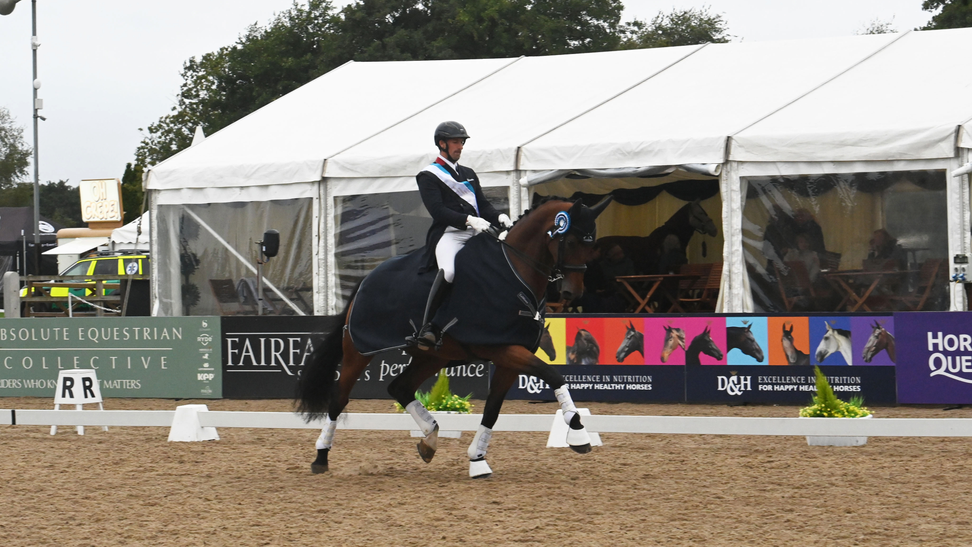 Michael Eilberg wearing a navy tailcoat with red trim with a winners sash riding in the prize giving on MSJ Dante VX